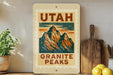 A framed poster of the Utah Granite Peaks hangs on a wall, surrounded by kitchen utensils and a potted plant.