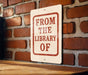 A sign on a brick wall that reads "FROM THE LIBRARY OF".