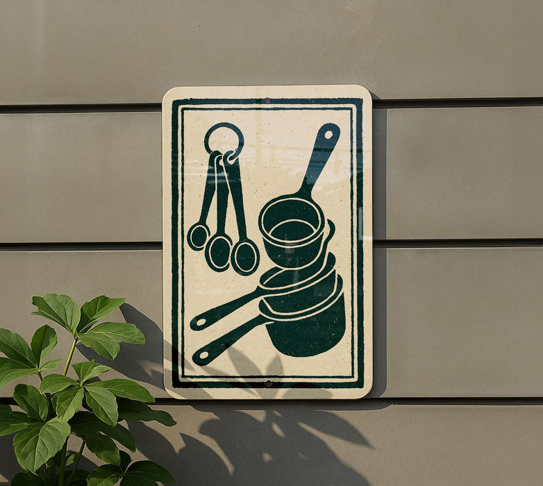 a sign with a pictogram of kitchen utensils, including measuring spoons and a ladle, mounted on a wall.