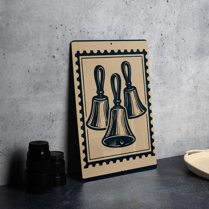 a framed illustration of three bells on a wall, with a stack of black camera lenses placed next to it.