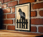A black and white cat silhouette is displayed on a wooden surface against a brick wall.