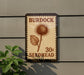 A postage stamp-like sign with the text "Burdock 30c Seedhead" and an illustration of a thistle flower.