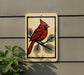 a sign with a red cardinal perched on a branch, set against a gray wall.