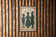 A framed image of three people, likely a group of three individuals, is displayed on a wooden wall.