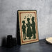 A framed illustration of three people, likely depicting a family or group of friends, is displayed on a table against a gray wall.