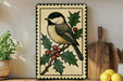 A decorative metal sign featuring a black-and-white bird perched on a branch with berries, surrounded by holly leaves and a pine cone.