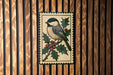 A decorative bird illustration is displayed on a wooden wall, surrounded by holly leaves and berries.