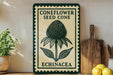 a vintage-style sign with the text "CONEFLOWER SEED CONE ECHINACEA" and a detailed illustration of a coneflower seed cone. The sign is displayed on a shelf next to a wooden cutting board and a potted plant, creating a rustic and homey atmosphere.