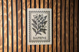 a sign with a floral design and the word "DAPHNE" printed on it, mounted on a wooden wall.