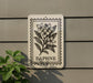 a sign with a floral design and the word "DAPHNE" printed on it, mounted on a wall next to a plant.