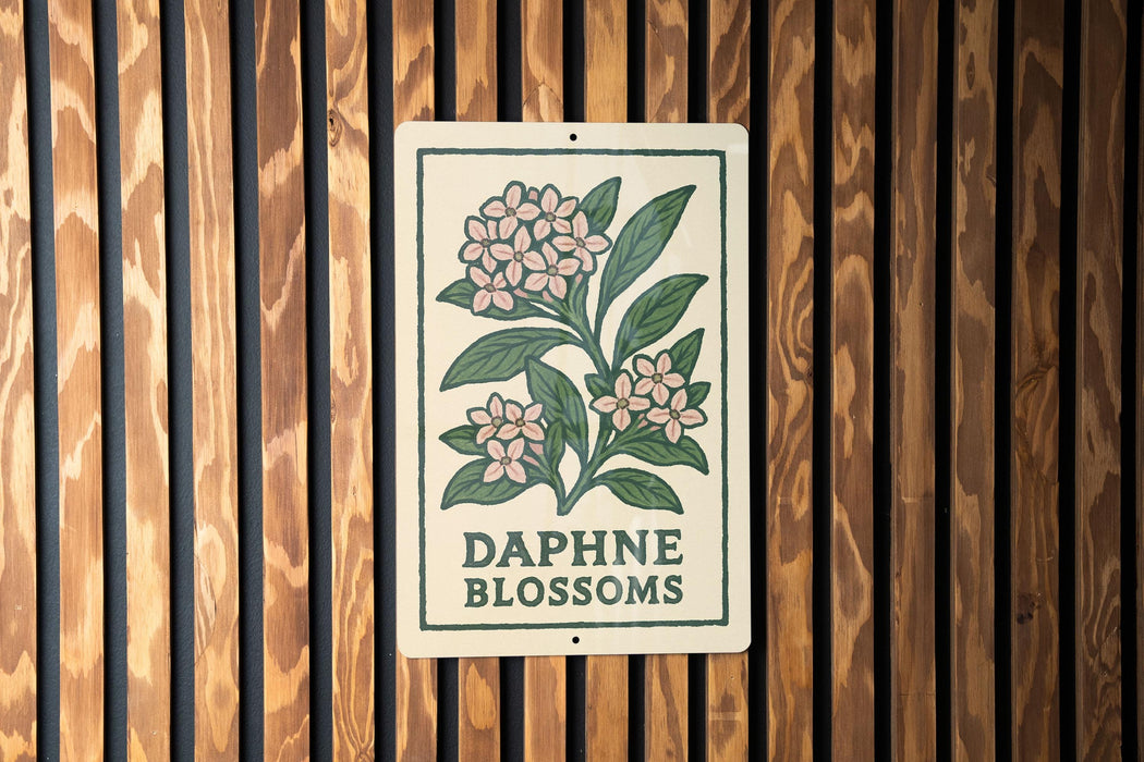 a sign with a floral design and the text "Daphne blossoms" on it, mounted on a wooden wall.
