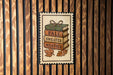 A framed image of a stack of books with the text "FALL WEATHER" written on them, along with autumn leaves.