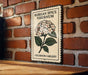 A decorative metal sign with a floral illustration and text, mounted on a brick wall.