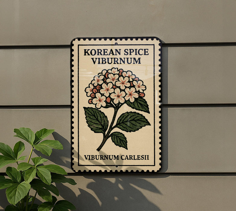 A decorative sign with a floral design and text, mounted on a wall next to a plant.