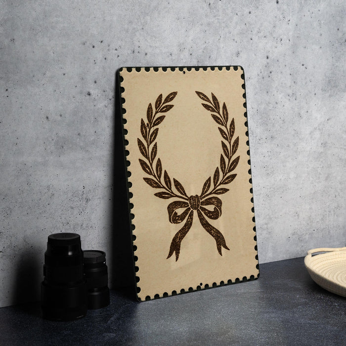 a framed picture of a laurel wreath on a wall, with a stack of black camera lenses placed next to it.