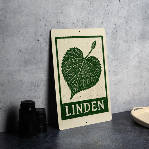 a sign with a green leaf design and the word "LINDEN" written on it, placed on a countertop next to some black camera lenses.