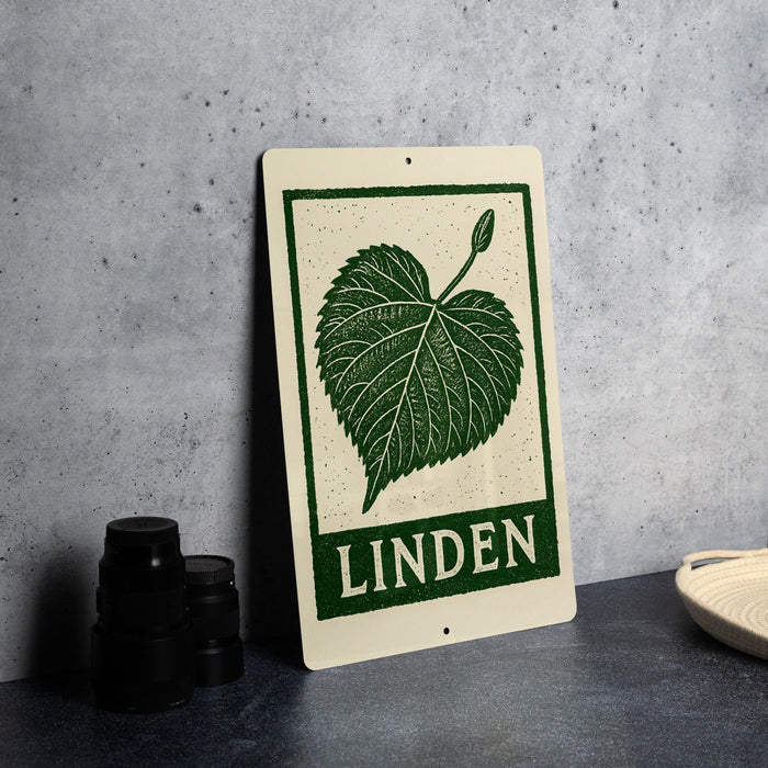 a sign with a green leaf design and the word "LINDEN" written on it, placed on a countertop next to some black camera lenses.