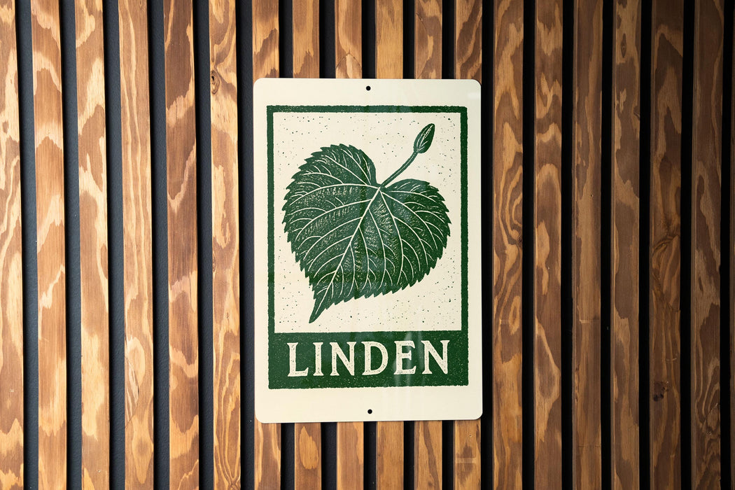 A metal sign with a green leaf and the word "LINDEN" printed on it is mounted on a wooden wall.