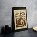 a framed illustration of a church with a steeple, depicting a rural landscape with mountains and trees.