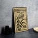a framed stamp with a plant illustration and text, placed on a table next to some black camera lenses.