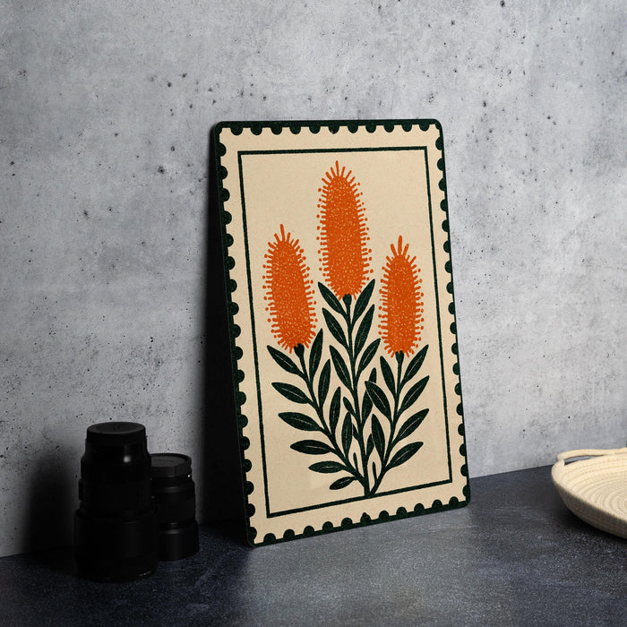 a framed artwork depicting orange flowers with green leaves, placed on a table next to a stack of black camera lenses.