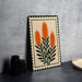 a framed artwork depicting orange flowers with green leaves, placed on a table next to a stack of black camera lenses.