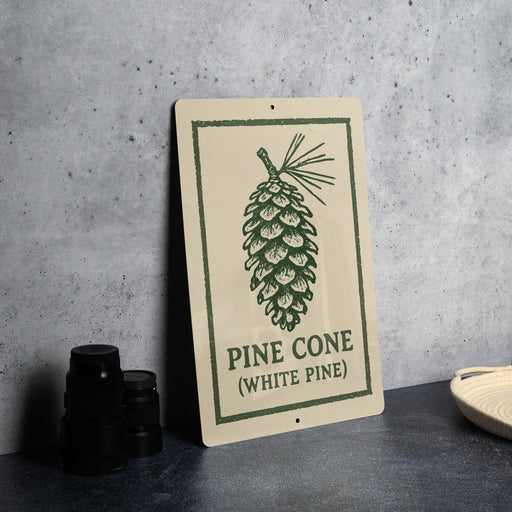 A sign with a pine cone illustration and the text "PINE CONE (WHITE PINE)" is displayed on a table.