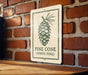 A sign with a pine cone illustration is mounted on a brick wall.