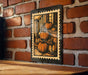 A framed illustration of three pumpkins is displayed on a brick wall, with a wooden table below it.