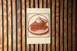 A sign featuring a pie with whipped cream on top, mounted on a wooden wall.