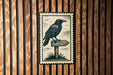 A black and white illustration of a crow perched on a wooden signpost, with birds in the background.