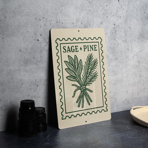 a sign with the text "SAGE + PINE" and an illustration of a plant, placed on a table next to some black containers.