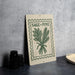 a sign with the text "SAGE + PINE" and an illustration of a plant, placed on a table next to some black containers.