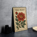 A framed print of a red peony flower is displayed on a table, with a stack of black camera lenses and a white dish visible to the side.