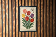 A colorful postage stamp featuring a bouquet of tulips is displayed on a wooden wall.