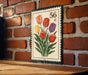 A decorative metal stamp with a floral design, featuring a group of six tulips in various colors, is displayed on a brick wall.