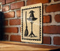 A sign featuring a witch's hat and broom is mounted on a brick wall.