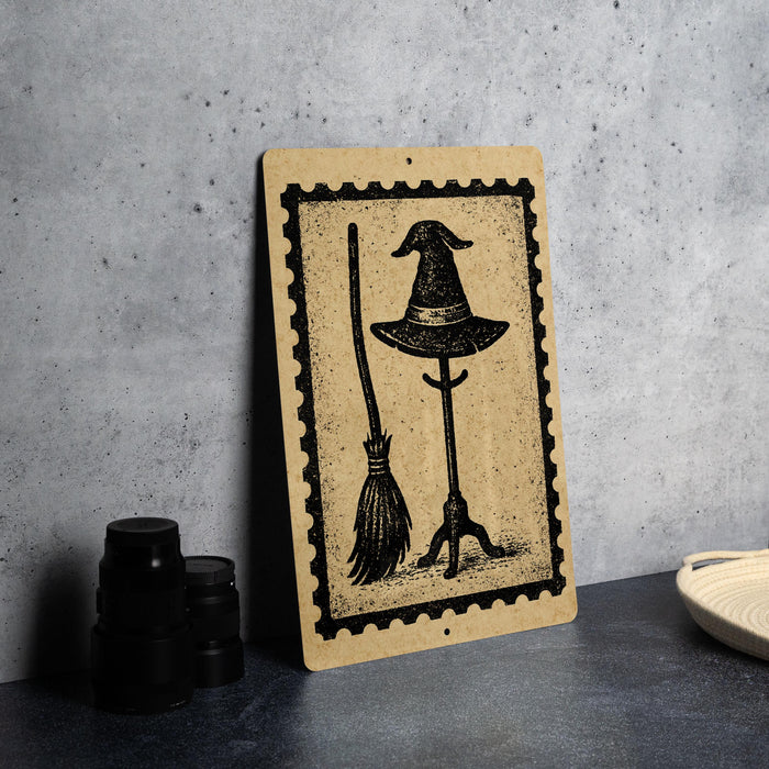 A wooden sign with a witch's hat and broom on it, placed on a table next to some black objects.