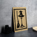 A wooden sign with a witch's hat and broom on it, placed on a table next to some black objects.
