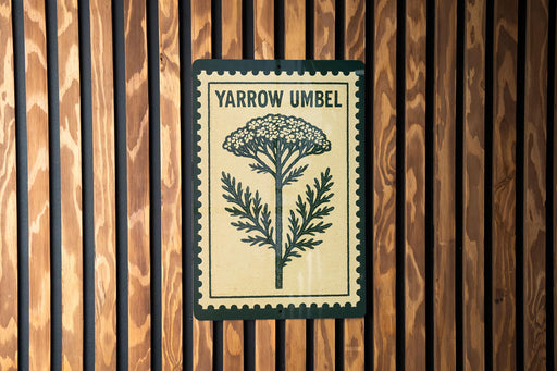 A sign with the word "YARROW UMBEL" printed on it, mounted on a wooden wall.