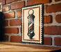 A metal sign featuring a barber pole is mounted on a brick wall.