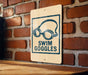A sign with a pair of goggles on it is mounted on a brick wall.