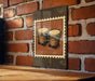 A framed image of two conga drums is hanging on a brick wall.
