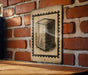 a brick wall with a framed illustration of a rectangular object, possibly a book or a box, hanging on it.