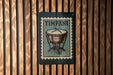 A metal sign with a drum design is mounted on a wooden wall.
