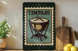 A framed illustration of a drum is displayed on a shelf, accompanied by a wooden cutting board and a potted plant.