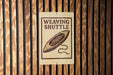 A sign that reads "Weaving Shuttle" is mounted on a wooden wall.