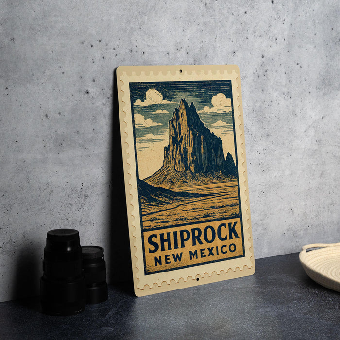 A framed illustration of a mountain with the text "SHIPROCK NEW MEXICO" on it, placed on a table next to some black camera lenses.