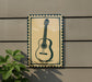 a guitar sign on a wall, with a plant to the left of the sign.
