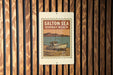 A metal sign with a vintage-style illustration of a boat on a beach, mounted on a wooden wall.